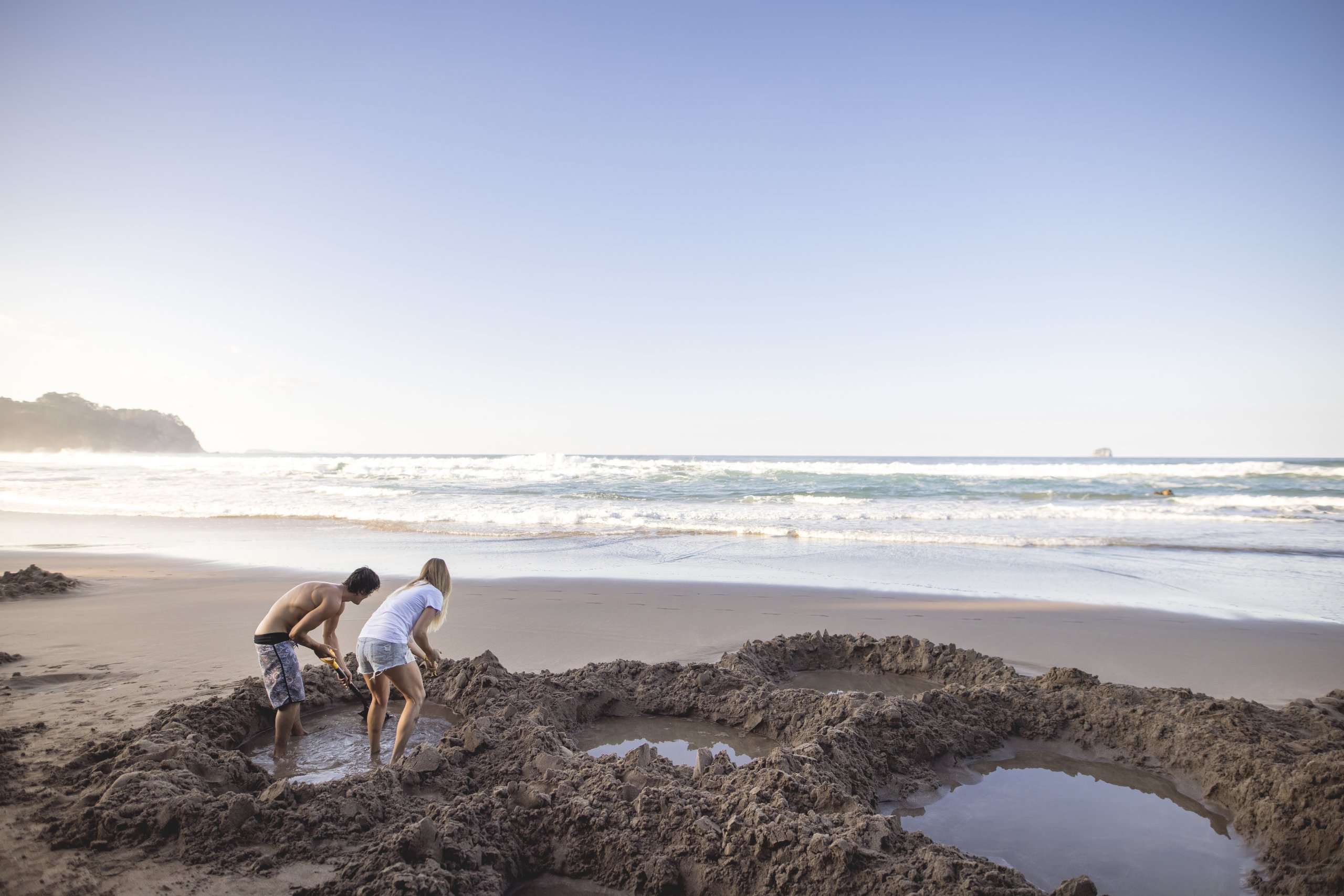 Two tourists digging own pools on Coromandel's Hot Water Beach